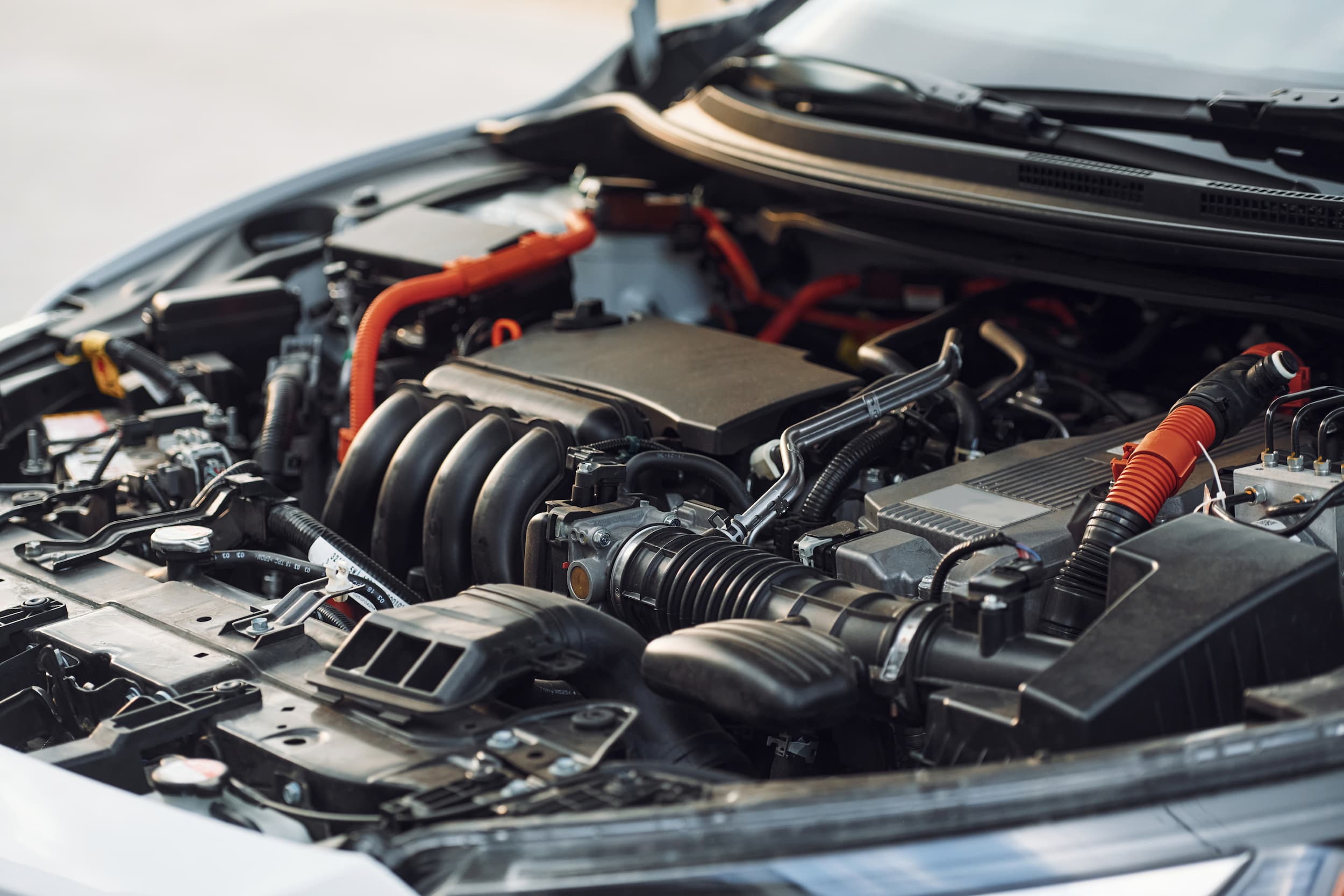 A close-up view of a car engine with various components, including hoses, air intake, and wiring, under an open hood.